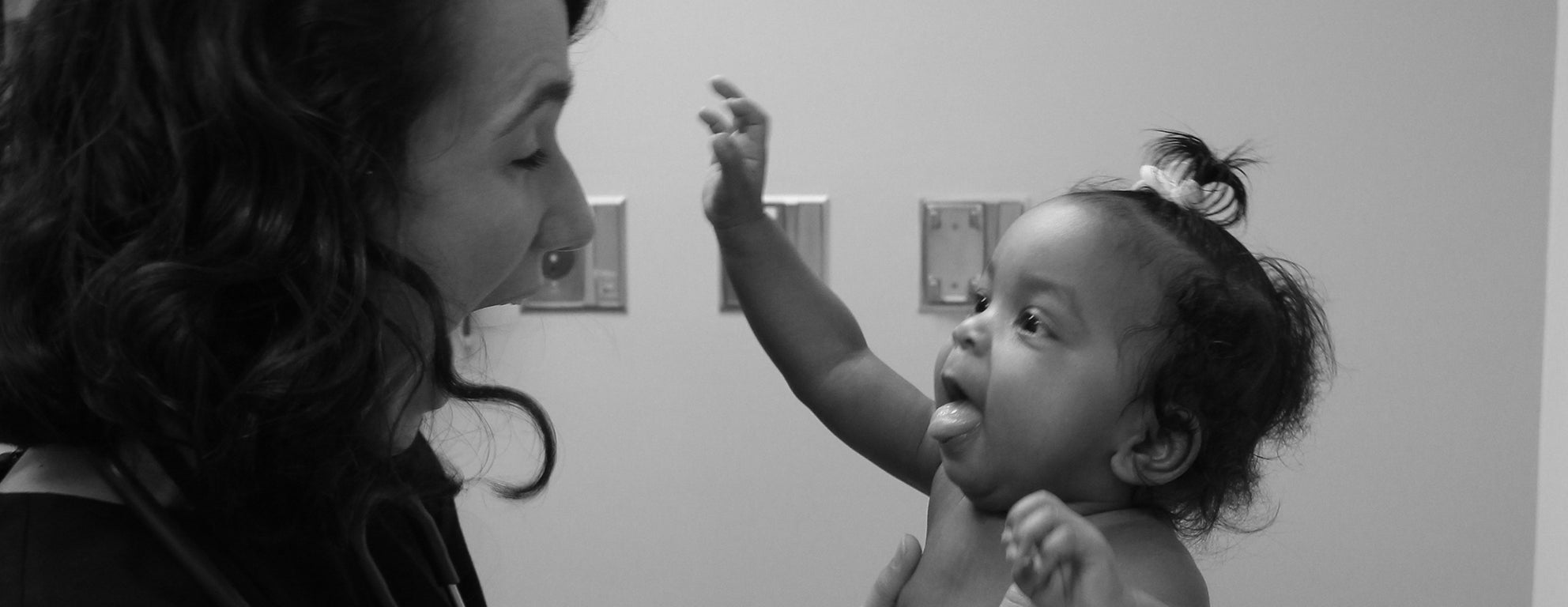 Black and white photo of Lucy Marcil making a silly face while holding a baby in the clinic